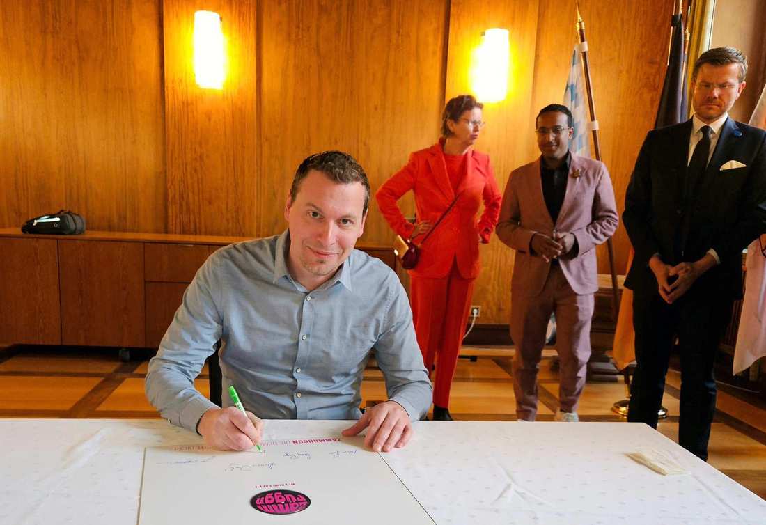 Kai Stähler unterzeichnet im Sitzen eine Urkunde des Demokratie-Bündnisses "Zammrüggn".