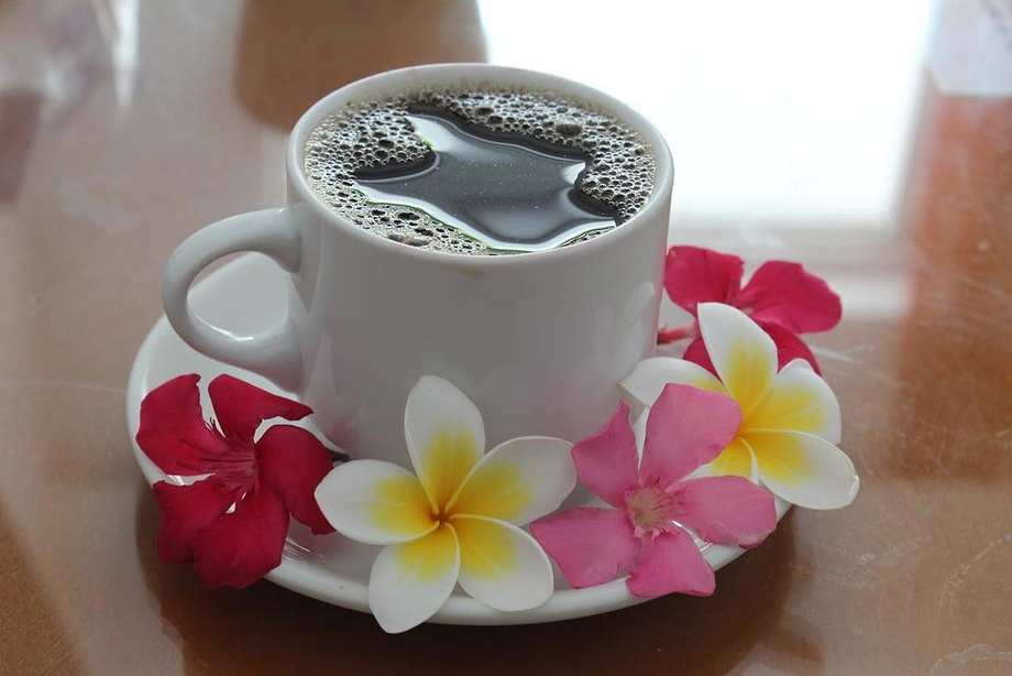 Eine Tasse mit Kaffee. Auf der Untertasse sind Blüten drapiert.