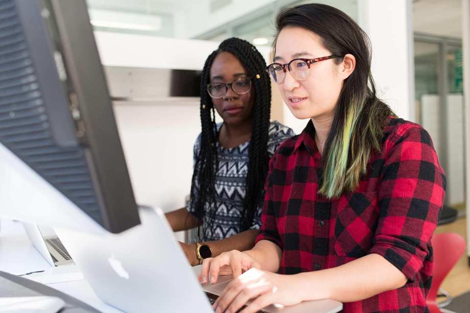 An einem Computerbildschirm sitzen zwei junge Frauen.