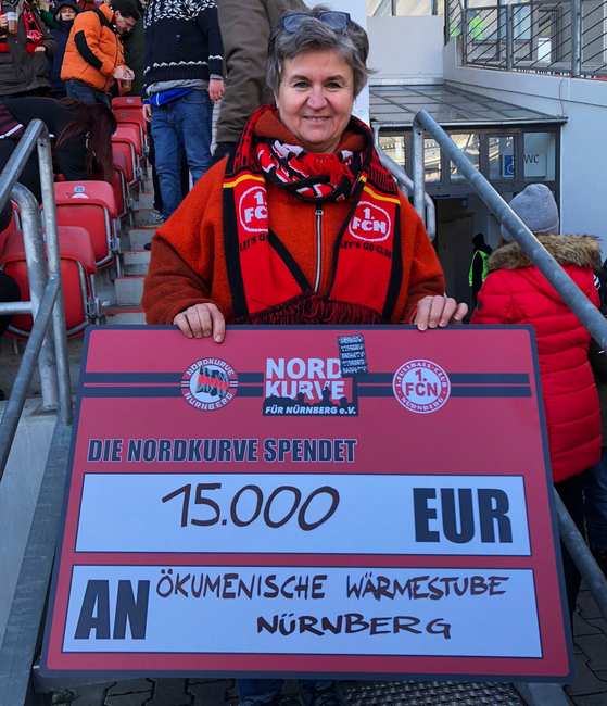 Einrichtungsleiterin Manuela Bauer steht im Stadion mit einem Scheck über 15.000 Euro.