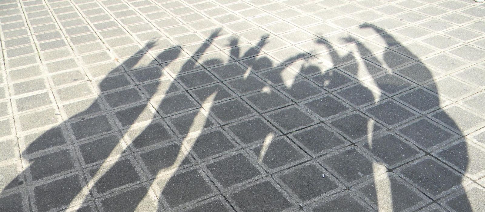 Die Schatten von einer Gruppe von Leuten die ihre Hände in der Luft haben 