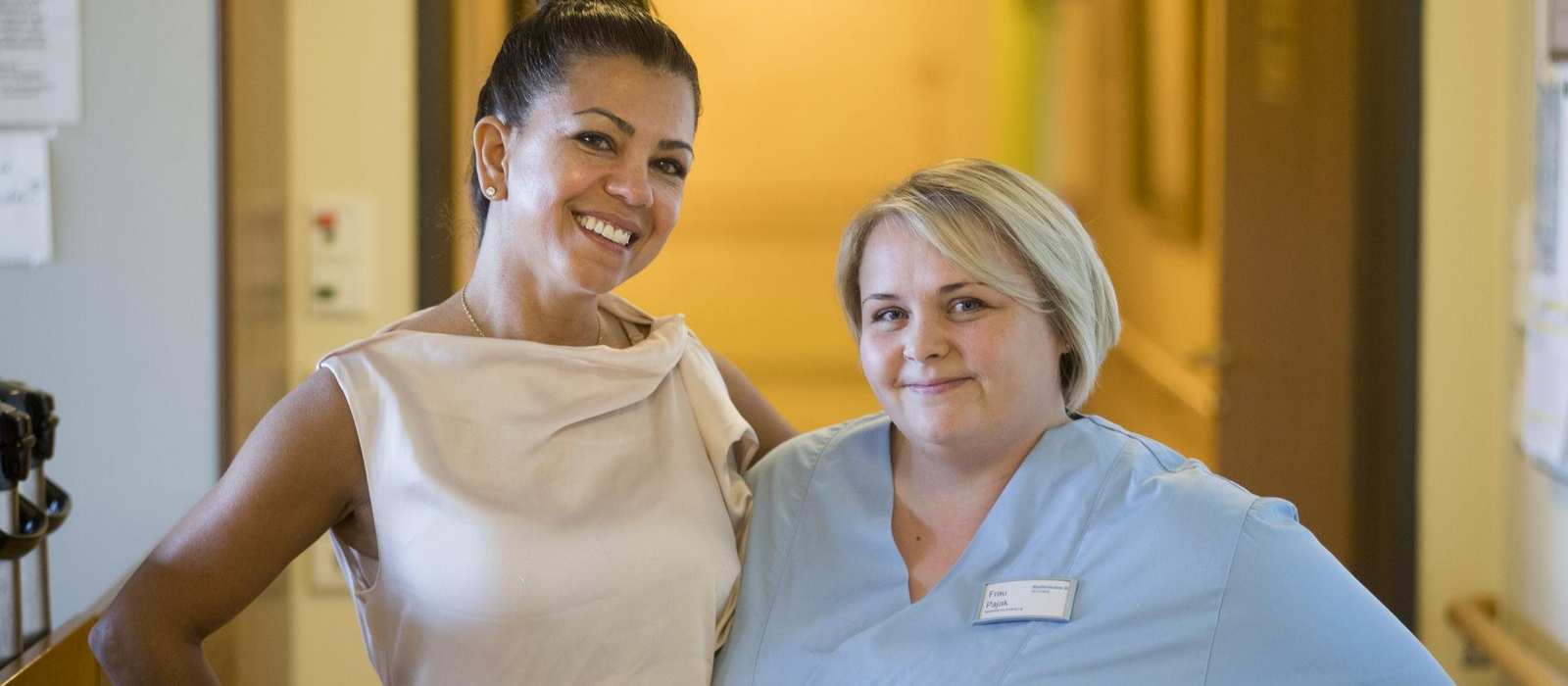 Zwei Frauen, eine Pflegedienstleitung und eine Pflegefachkraft, stehen nebeneinander und lächeln