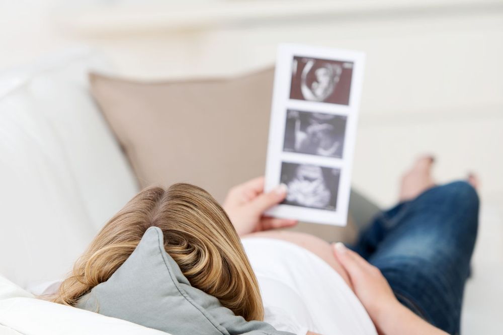 Eine schwangere Frau liegt auf dem Sofa und betrachtet Ultraschall-Fotos
