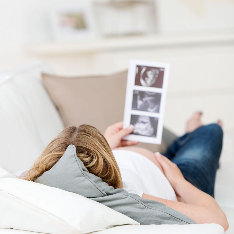 Eine schwangere Frau liegt auf dem Sofa und betrachtet Ultraschall-Fotos