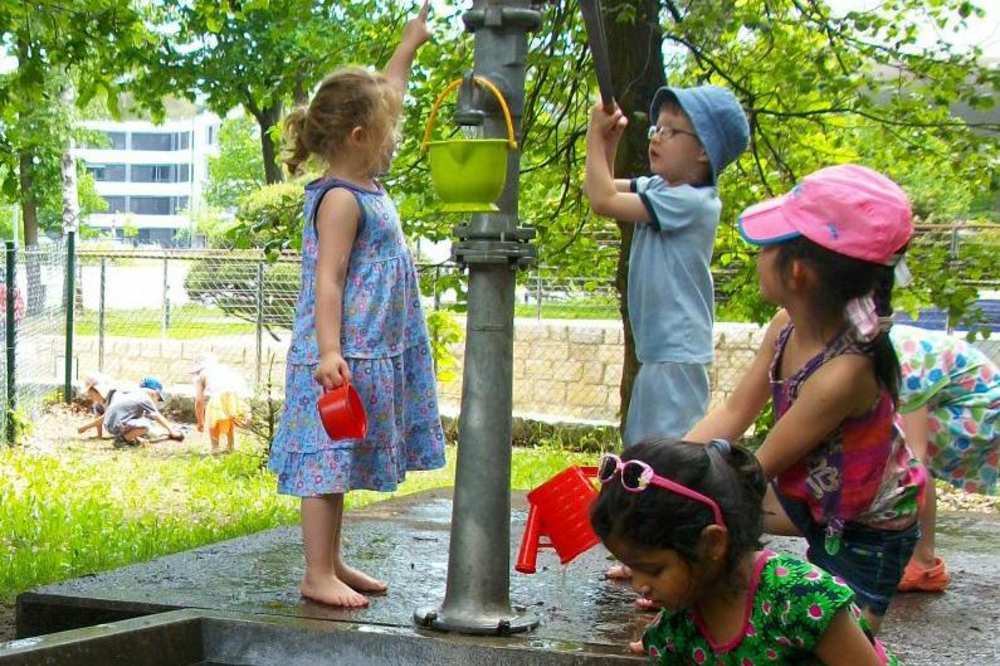 Vier Kinder spielen an einem Wasserspielplatz bzw. Brunnen.