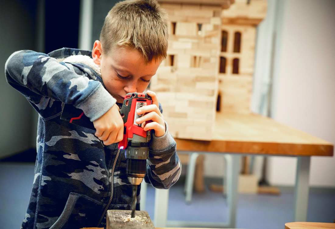 Ein Junge bohrt konzentriert mit einem neuen Holzbohrer an einem Holzklotz