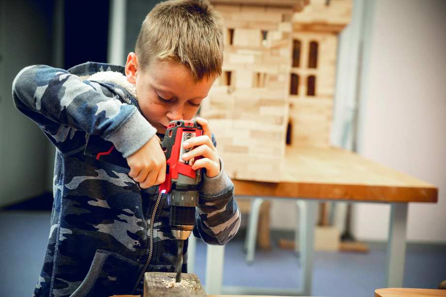 Ein Junge bohrt konzentriert mit einem neuen Holzbohrer an einem Holzklotz
