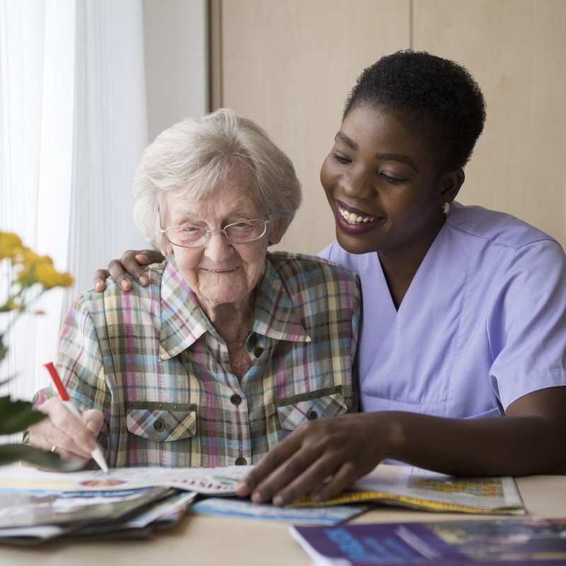 Eine Pflegerin und eine ältere Dame machen gemeinsam Kreuzworträtsel.