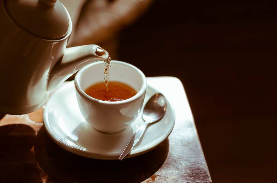 Aus einer Porzellankanne wird Tee in eine weiße Teetasse eingegossen.