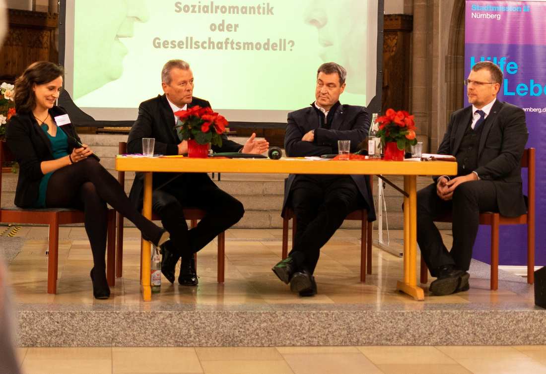 An einem Tisch sitzen Ulrich Maly, Markus Söder. An den beiden Rändern die Moderatoren*innen Sigfried Grillmeyer vom Caritas-Pirckheimer-Haus und Tabea Bozada von der Stadtmission Nürnberg.