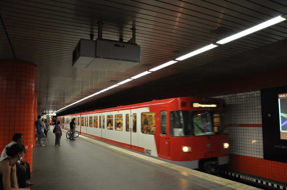 In einer U-Bahnstation sitzen einige Menschen auf Sitzen, eine rote U-Bahn ist eingefahren.
