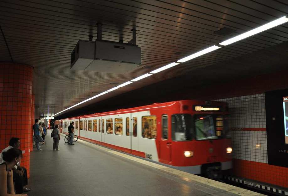 In einer U-Bahnstation sitzen einige Menschen auf Sitzen, eine rote U-Bahn ist eingefahren.