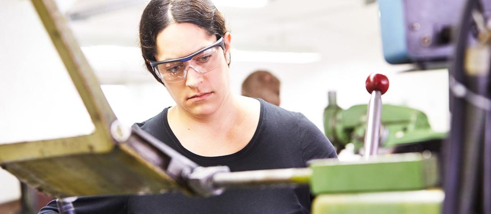 Eine junge Frau steht mit Schutzbrille an einer Maschine.
