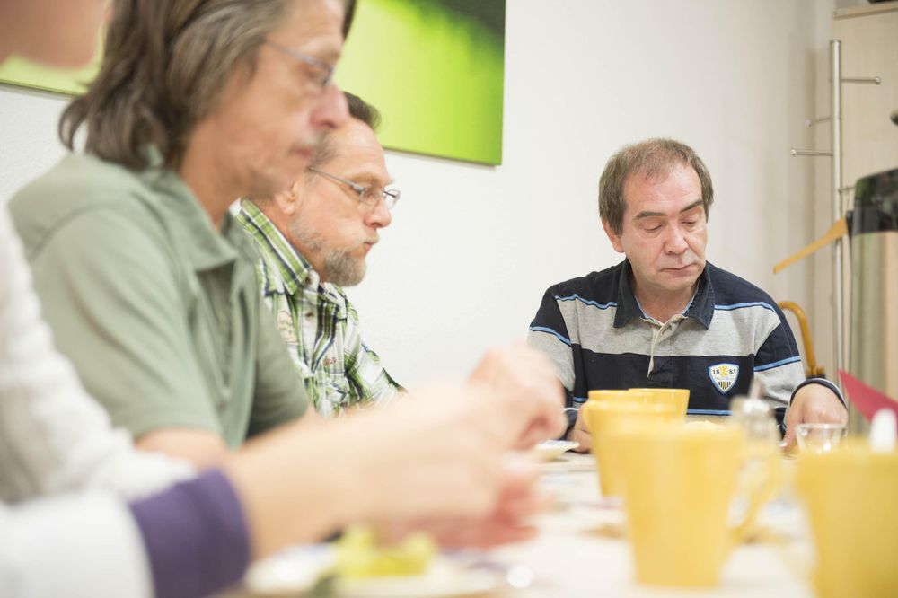 Drei Männer sitzen an einem Frühstückstisch mit gelben Tassen.
